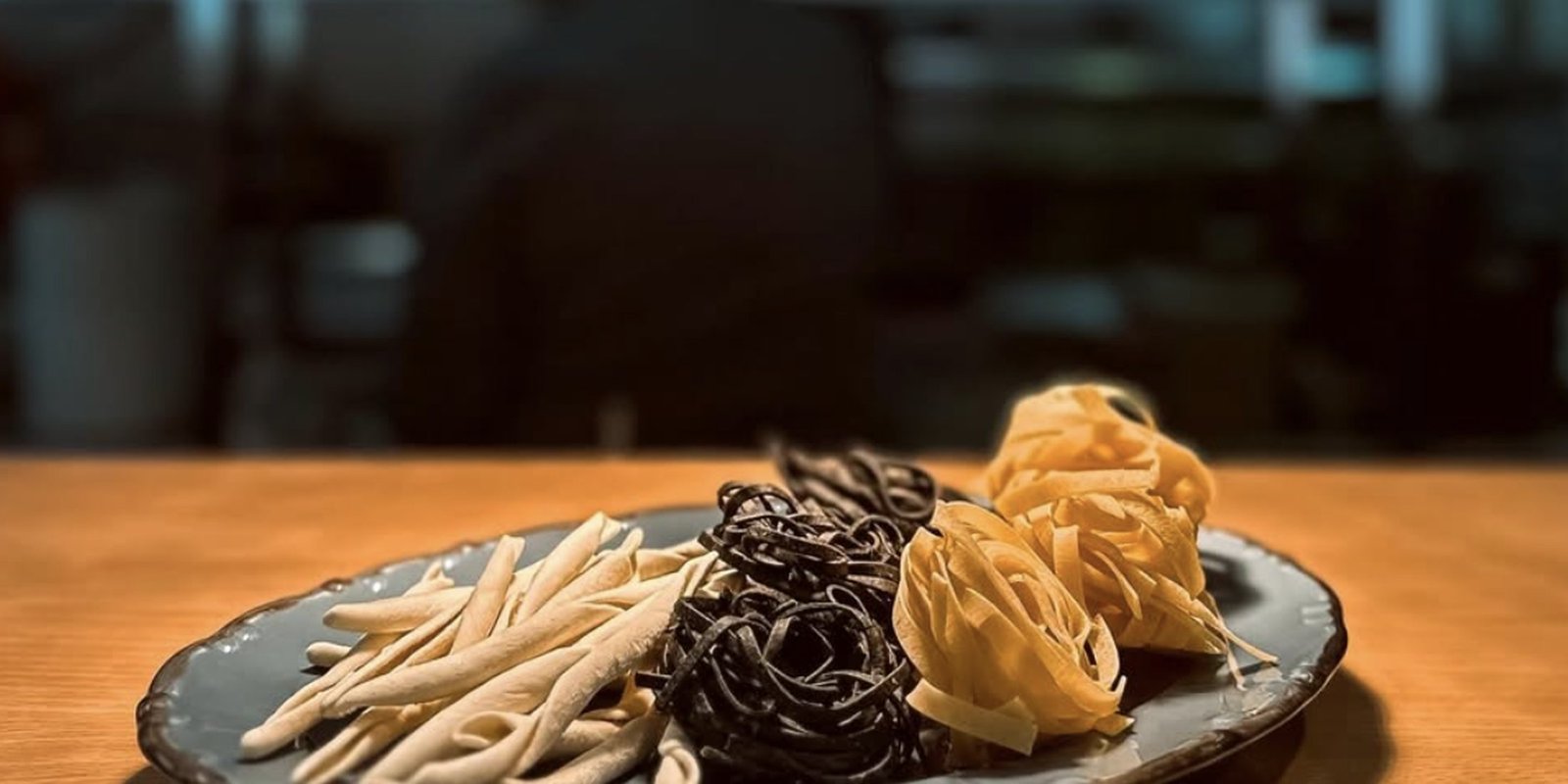 Plates of squid ink tagliatelle and pasta on a dark table under low light