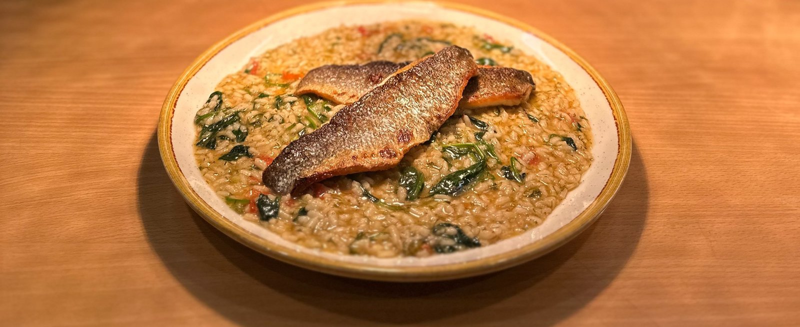 A plate of sea bass and spinach risotto on the warm wooden pass