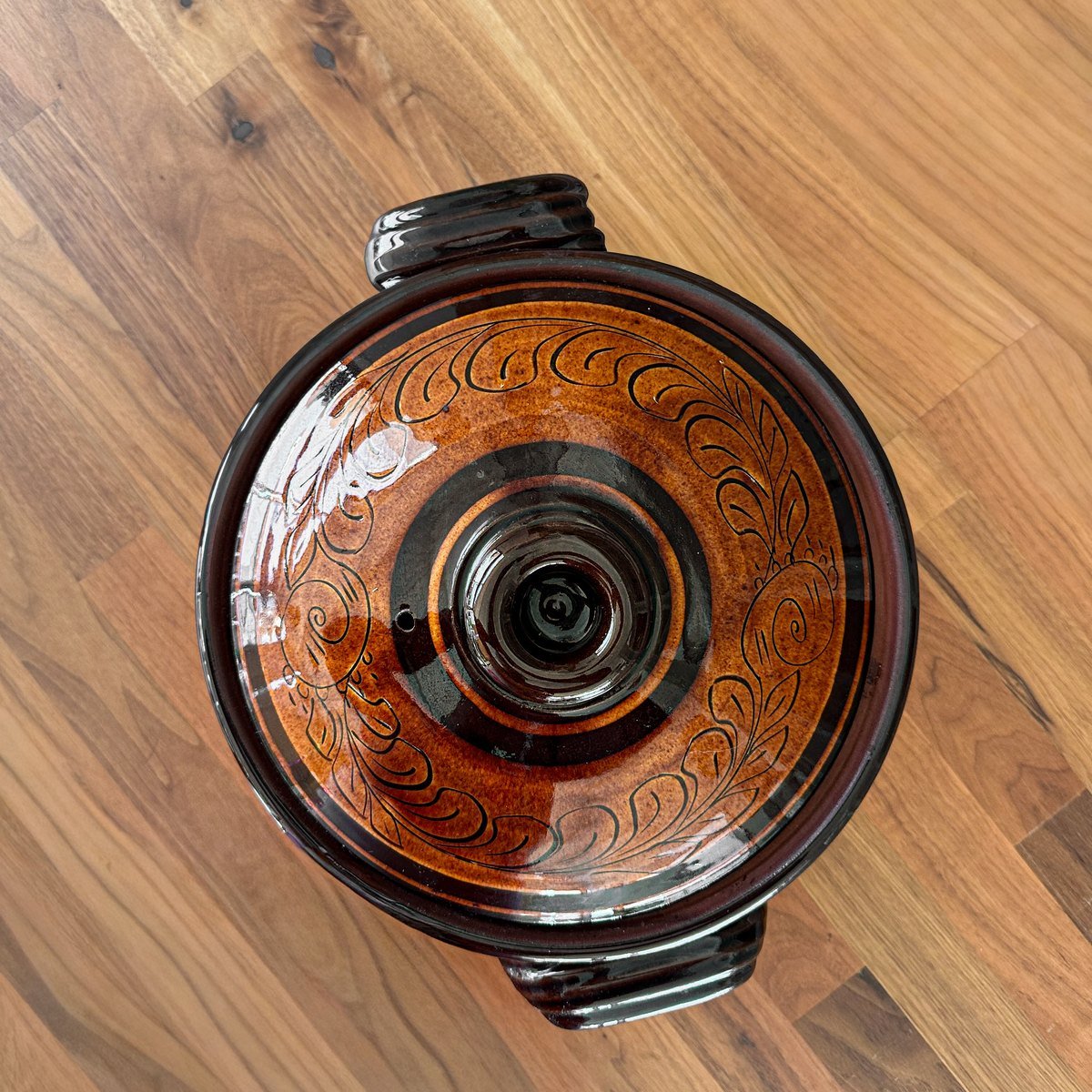 A glazed clay pot with its lid on, hand-painted with leaves